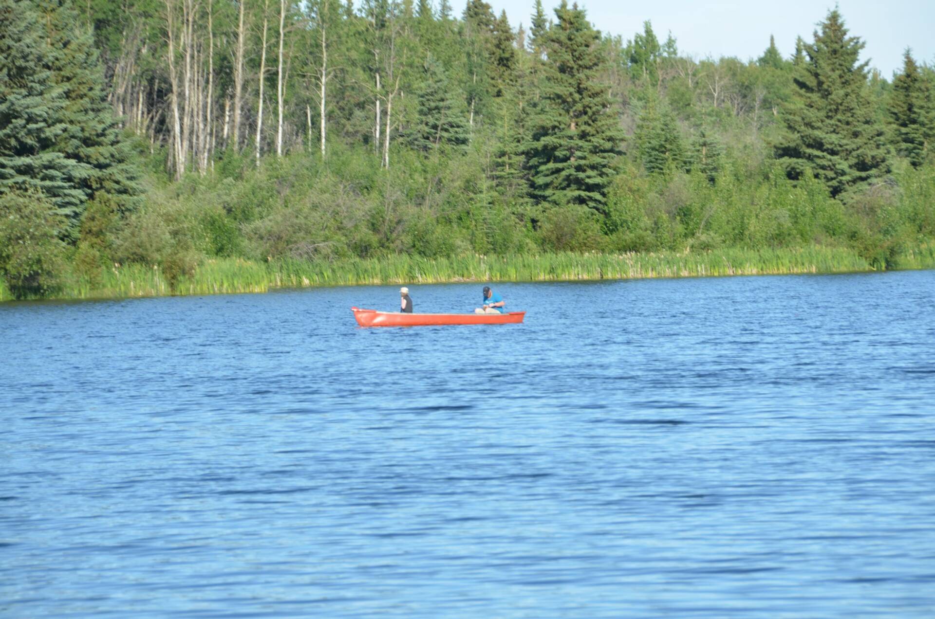 photo of lake in Alberta with 2 people in a red canoe in the distance