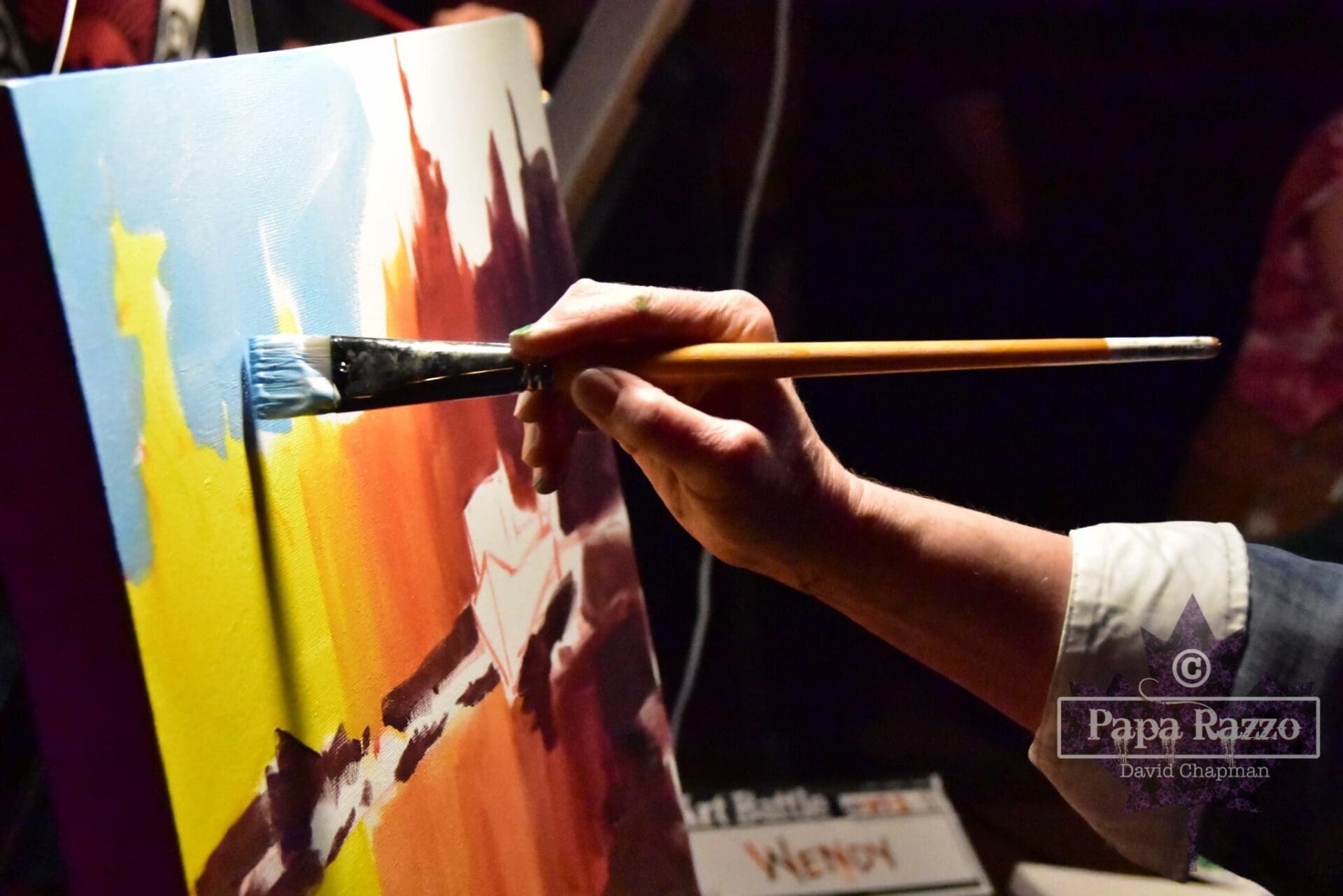 medium shot of an artist's hand and wrist holding a paintbrush and finishing a painting of an outdoor landscape 